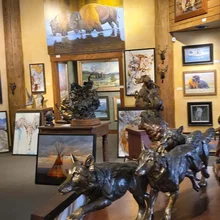 Bronze sculptures of wolves on a table in an art gallery with paintings of animals and landscapes on the walls
